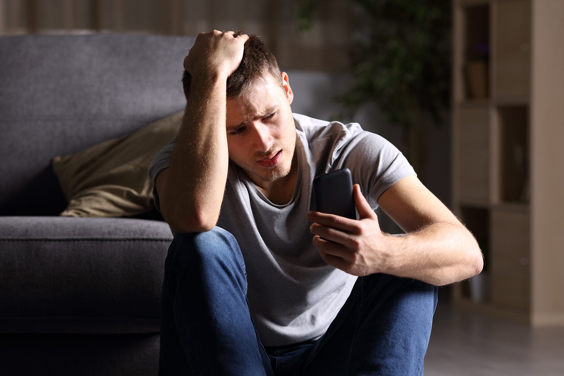 Distressed young man looking at a phone in a dark room.